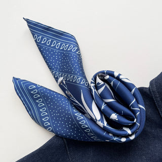 Blue Kyoto Blooms silk scarf with white polka dots, floral patterns and paisley designs, elegantly displayed against denim fabric