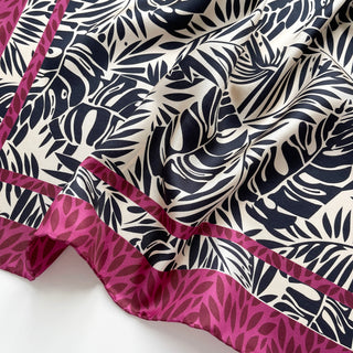 Luxury silk scarf featuring black tropical leaf pattern on light beige background with vibrant magenta border, showing elegant drape and hand-rolled edges
