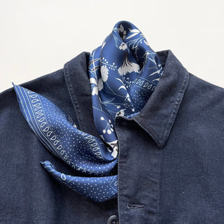 Blue Kyoto Blooms silk scarf with white floral pattern styled as a neckerchief with a denim shirt, showcasing the luxurious hand-rolled fabric and elegant design.