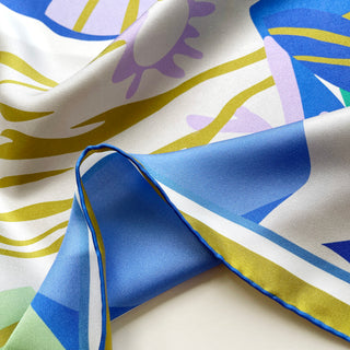 Close-up of a luxurious abstract lotus silk scarf in vibrant blue, teal, lilac, and mustard yellow patterns with hand-rolled edges, double-side printed.