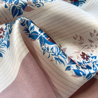 Blush pink silk scarf with vibrant blue and burgundy leaf pattern, showcasing the fabric's natural sheen and delicate texture in elegant folds.
