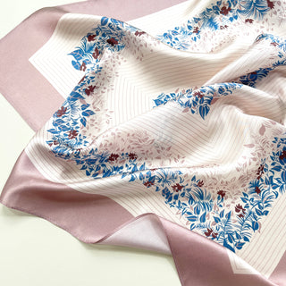 Blush pink silk scarf with elegant blue and burgundy leaf pattern, featuring a white center with geometric lines and floral border, displaying lustrous fabric texture