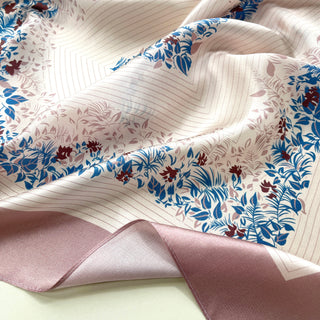 Blush pink silk scarf with elegant blue and burgundy floral leaf pattern border, showcasing lustrous fabric texture and delicate design details.