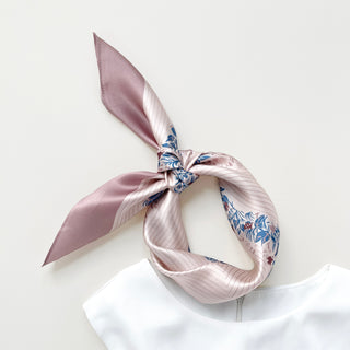 Blush pink silk scarf tied in a knot, featuring blue and burgundy leaf pattern design with subtle sheen against white background