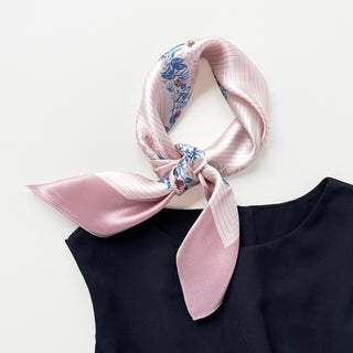Blush pink silk bandana scarf with blue and burgundy leaf pattern, elegantly knotted on navy top, showcasing sheen and luxurious texture