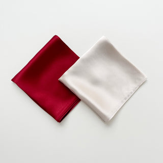 Two folded square silk scarves, one red and one pink beige, on a light grey background