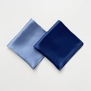 Two folded square silk scarves, one navy and one sky blue, on a light grey background