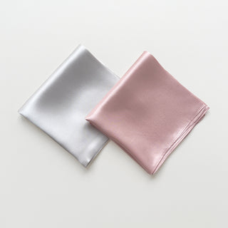 Two folded square silk scarves, one beigei grey and one pink, on a light grey background