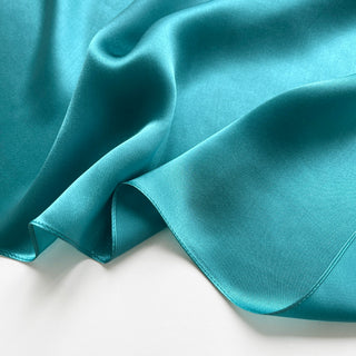 Close-up of a teal silk satin scarf with smooth, lustrous finish showing the scarf's soft texture and rich colour