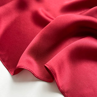 Close-up of a red silk satin scarf with smooth, lustrous finish showing the scarf's soft texture and rich colour
