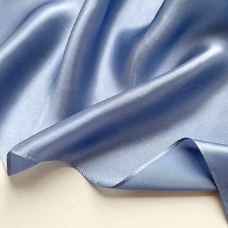 Close-up of a sky blue silk satin scarf with smooth, lustrous finish showing the scarf's soft texture and rich colour