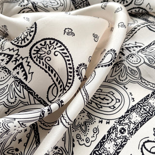 Light beige silk scarf with black paisley pattern, draped to showcase its lustrous sheen and intricate traditional design details