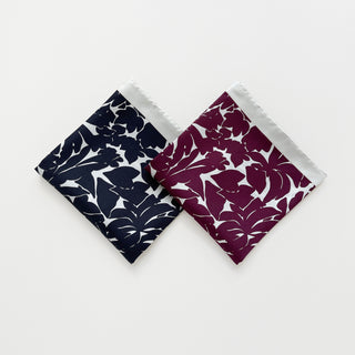 Two folded silk scarves in burgundy and black floral print with ice white border, 65cm square.