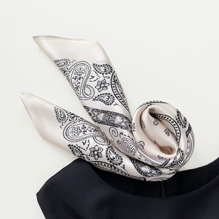 Light beige silk bandana scarf with elegant black paisley pattern, draped with a natural sheen showcasing its luxurious texture