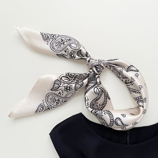 Light beige silk bandana scarf with black paisley pattern tied in a knot, showcasing its lustrous fabric and elegant design