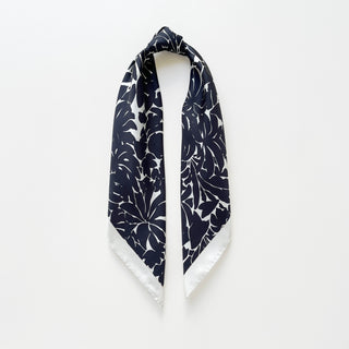 Luxury silk scarf in black floral print with ice white border on a light grey background.