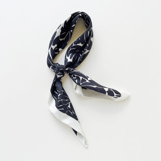 Luxury silk scarf in black floral print with ice white border on a light grey background.
