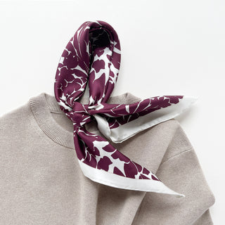 Luxury silk scarf in burgundy floral print with ice white border draped over a beige sweater on a light grey background