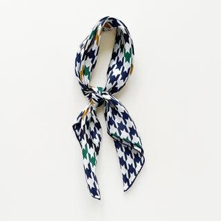 Luxury silk square scarf with navy, green, and gold houndstooth pattern on white background, elegantly knotted to showcase the hand-rolled edges