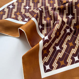 Luxury silk scarf with geometric 70s pattern in burgundy, amber and white with hand-rolled edges and white border on tan background