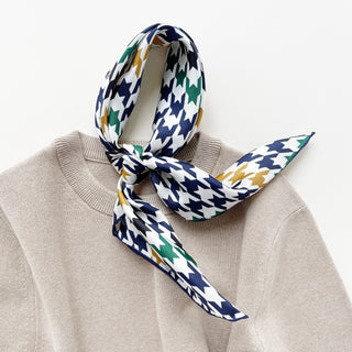 Luxury silk scarf with navy houndstooth pattern draped over a beige sweater on a light grey background