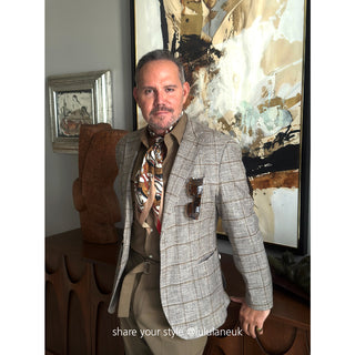 Designer outfit featuring a patterned tie with tiger motifs in earth tones, paired with a light grey checkered blazer against an abstract art backdrop