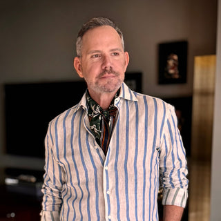 Men’s silk and cotton neck scarf in rich green with stylised bird print, styled with a white and blue striped shirt.