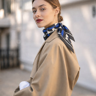 Woman wearing the 65cm English Seaside Pebble silk scarf with a classic camel trench coat.