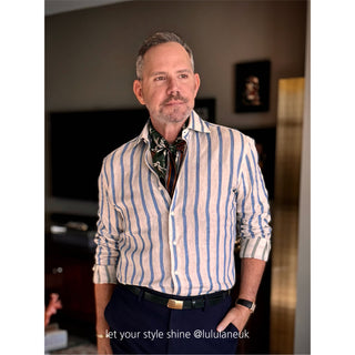 Men’s silk and cotton neck scarf in rich green with stylised bird print, styled with a white and blue striped shirt, navy blue trousers.