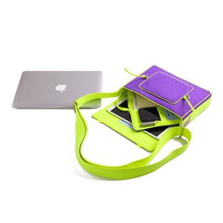 Purple messenger bag with bright green strap, shown open with smartphone and papers inside, displayed next to a MacBook for size comparison