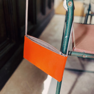 Bright orange small crossbody phone wallet with thin strap, partially unzipped showing gray interior, hanging on teal metal rack