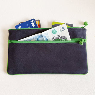 Navy double-zipper wallet with bright green trim showing credit cards in top compartment and £5 note in bottom compartment