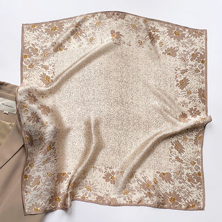 Square beige silk scarf with delicate brown floral pattern and gold accents along the border, displayed flat with subtle folds showing its luxurious sheen