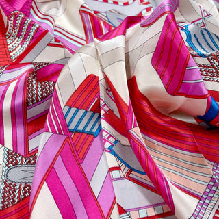 Luxurious silk scarf with vibrant magenta, red, and beige geometric city maze pattern, showcasing smooth fabric texture and elegant sheen