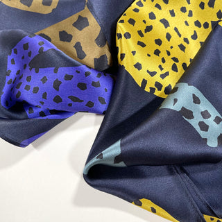 Silky leopard print scarf in navy blue with vibrant yellow, indigo blue, and bronze color blocks, showcasing luxurious fabric texture
