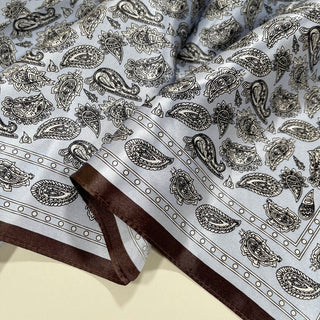 Pale blue silk bandana scarf with black paisley pattern and brown border, showing luxurious sheen and intricate design details