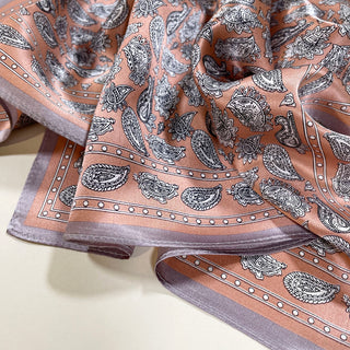 Luxurious pink silk scarf with black paisley pattern and lavender border, displaying elegant sheen and intricate design details