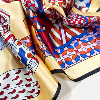 Luxurious 90cm silk scarf with medieval carnival pattern featuring yellow border and vibrant red, blue, and pink geometric designs with shimmering fabric texture