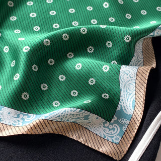 Green silk bandana with white floral pattern, featuring decorative blue and beige border detail, showing the scarf's luxurious sheen and texture