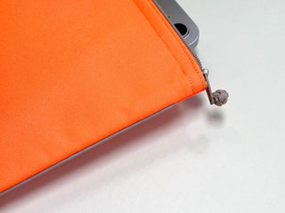 Vibrant neon orange recycled waterproof iPad case with silver YKK zipper detail, showing corner of iPad device inside the eco-friendly sleeve