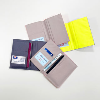 Four minimalist recycled passport holders displayed open, showing interior card slots and compartments in navy, beige, and neon yellow colors with neat piping details.