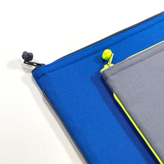 Two recycled waterproof iPad cases - vibrant blue with black zipper pull and gray with neon yellow trim, showing detailed piping and YKK zippers