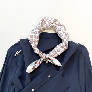 Cream silk neckerchief with brown medal pattern displayed on navy blue shirt, tied elegantly at neck with decorative border detail
