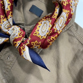 Red silk neckerchief with gold and white paisley pattern styled with navy blue accent, worn with beige jacket for elegant men's fashion.
