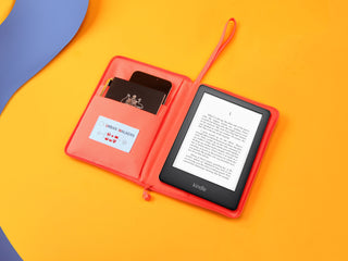 Bright coral recycled Kindle case opened on yellow background, showing Kindle e-reader, passport, and card slots in an all-in-one travel organizer design.