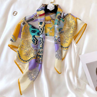 Luxury silk scarf with vintage-inspired pattern in yellow, lilac, and teal, displayed draped on a hanger with decorative white flower accent