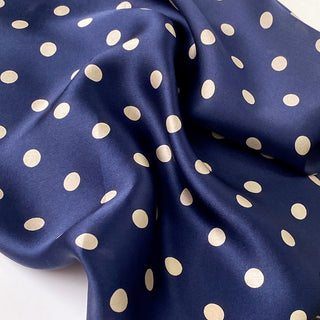 Navy blue silk scarf with elegant champagne polka dots, showcasing luxurious fabric texture with gentle folds highlighting the silky sheen