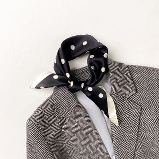 Navy blue silk scarf with white polka dots tied as a neckerchief, paired with a geometric patterned blazer for elegant styling.