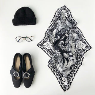Black silk bandana with white fern and monstera leaf pattern displayed with coordinating black accessories: knit beanie, eyeglasses, and embellished flat shoes