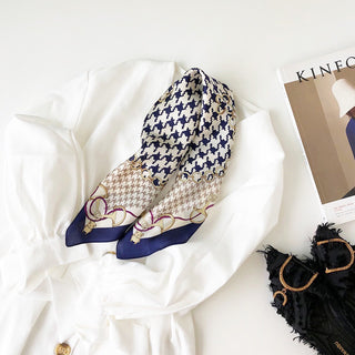 Indigo blue and cream houndstooth silk bandana scarf with decorative chain pattern border, displayed on white fabric next to fashion magazine